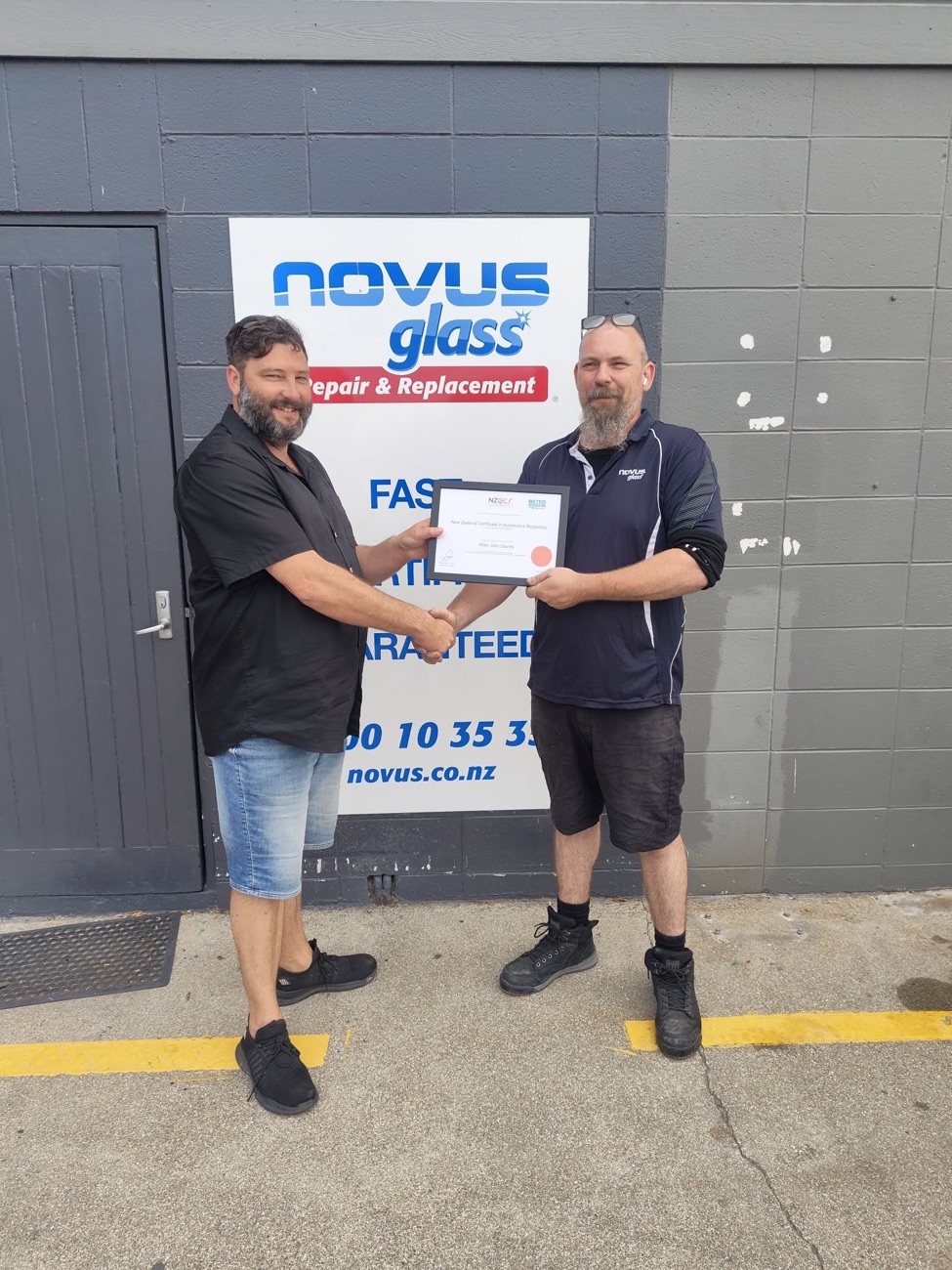 Al Davies receiving his automotive glass qualification in front of the Novus Glass sign